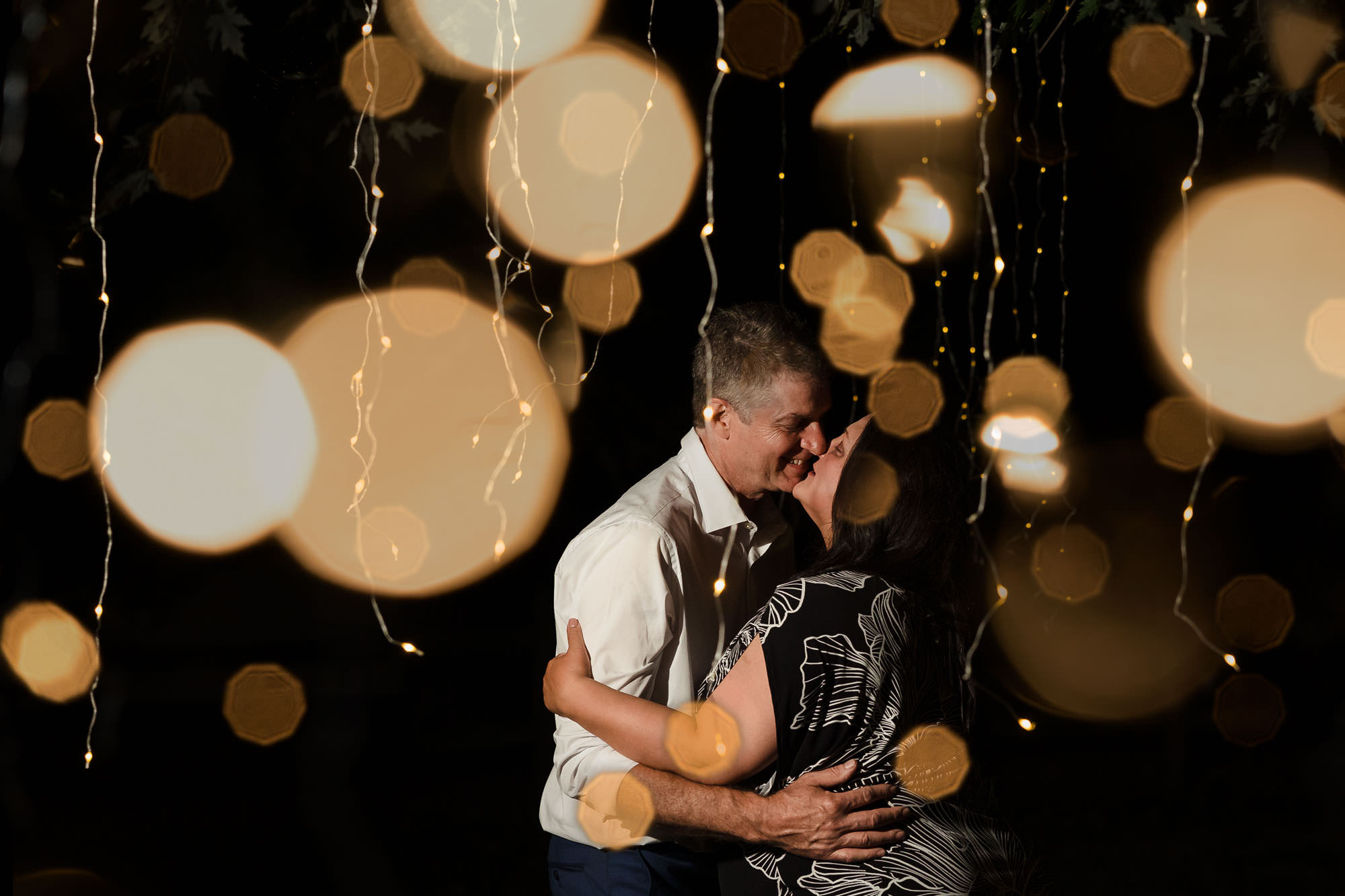 Couple kissing under bokeh string lights at night