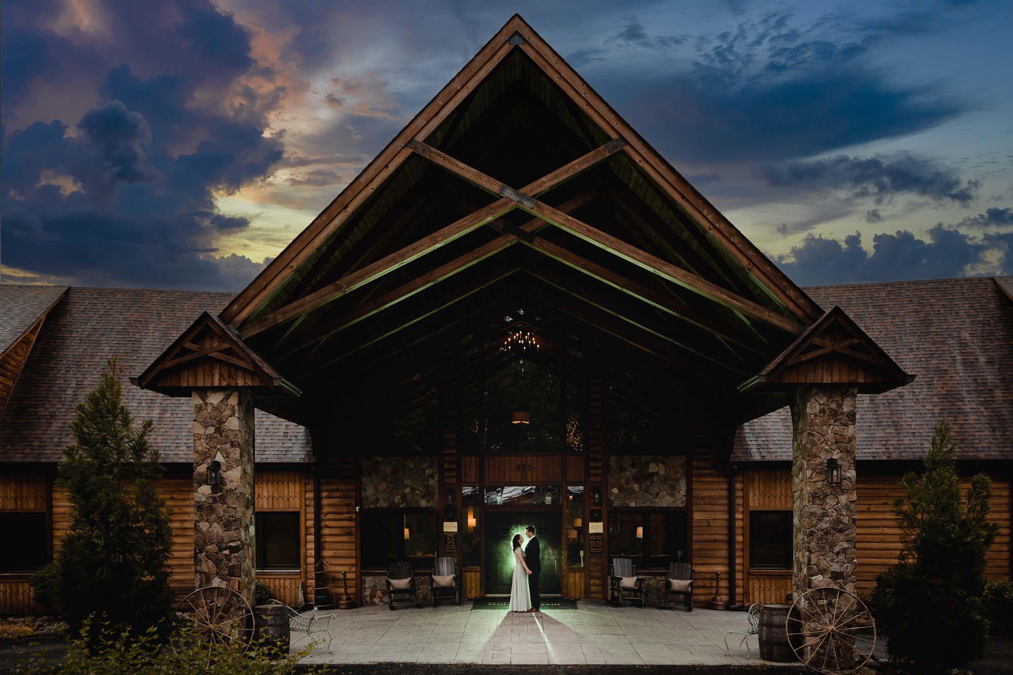 Wedding couple at rustic log cabin venue under dramatic twilight sky
