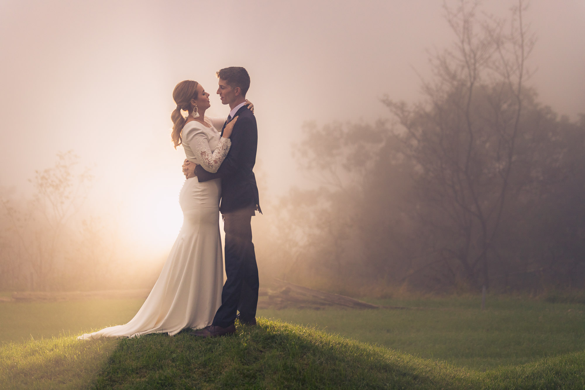 Bride and groom embracing on misty hilltop at golden hour