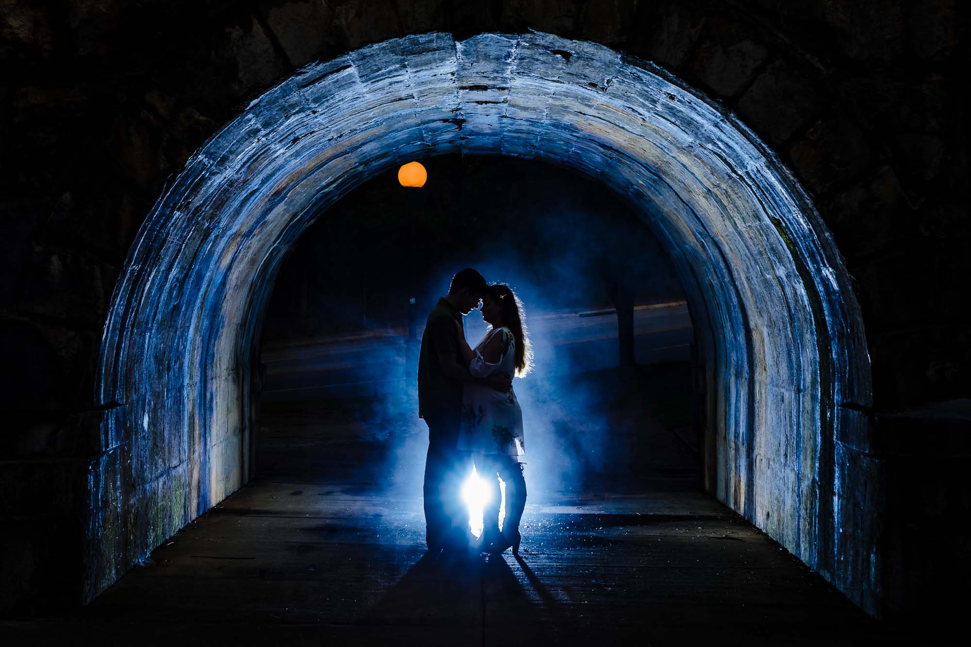 Couple silhouette in stone tunnel with blue smoke and light