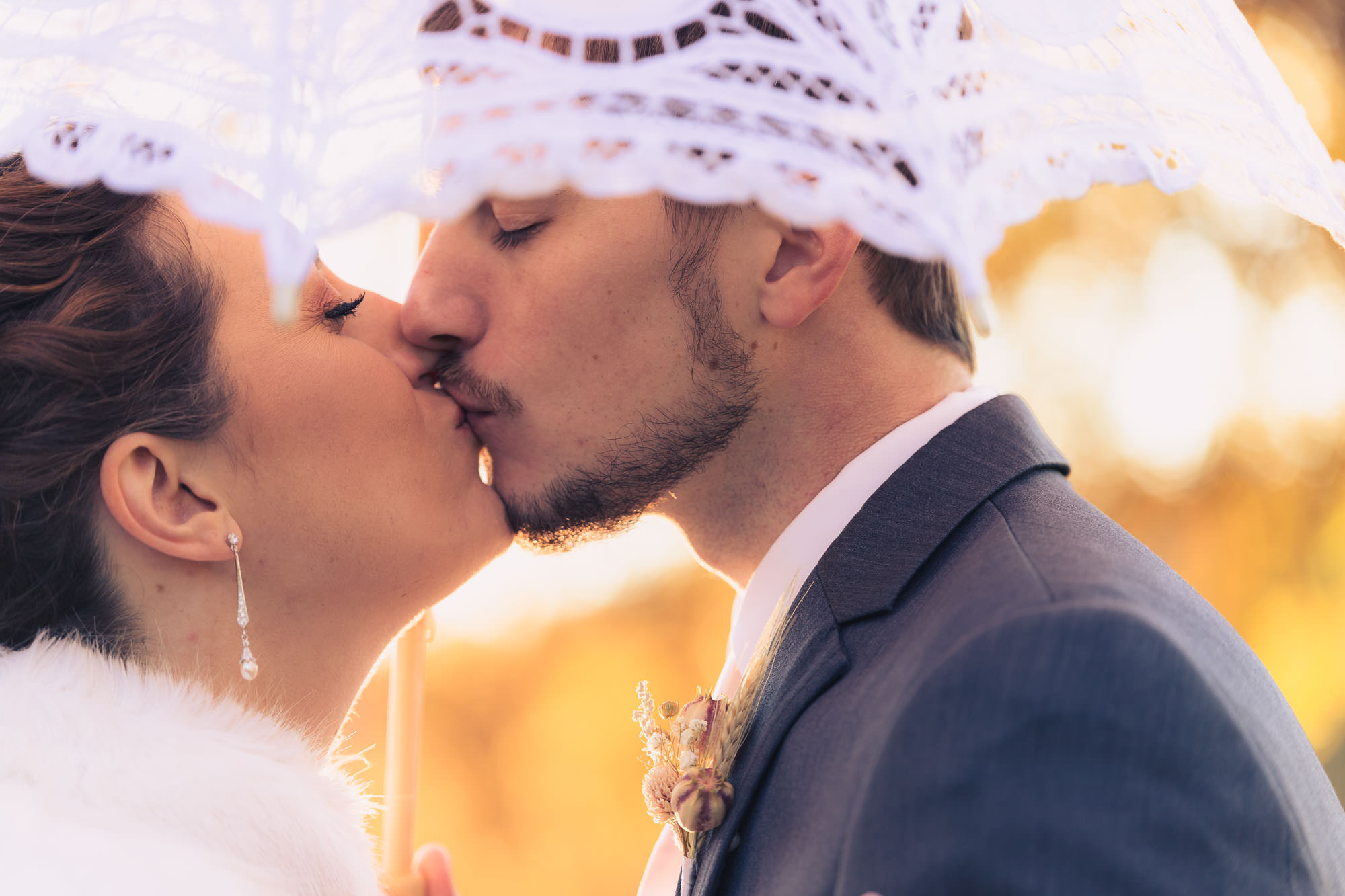 Bride and groom kissing under lace umbrella at sunset